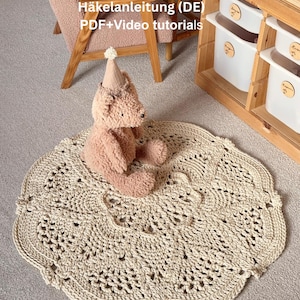 May include: A beige, round, crocheted rug with a scalloped edge. A plush teddy bear wearing a party hat sits on the rug. The rug has an openwork design. Text in the image reads "Häkelanleitung (DE) PDF+Video tutorials."