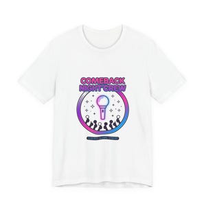 Può includere: T-shirt bianca con grafica circolare. La grafica presenta il testo "COMEBACK NIGHT CREW" in rosa e viola, un microfono, stelle e sagome di persone. Sotto la grafica c'è il testo "000 KST GLOBAL STREAM".