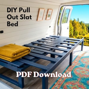 Peut inclure: Lit à lattes coulissant de bricolage peint en bleu foncé, avec une couverture jaune pliée. Le cadre du lit est à l'intérieur d'un van avec la porte ouverte, révélant une vue extérieure. Le texte "DIY Pull Out Slat Bed" et "PDF Download" sont visibles.