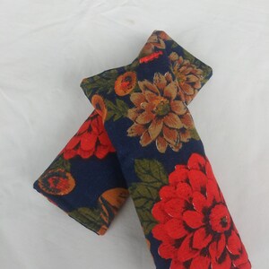 May include: Two blue fabric seatbelt pads with a floral pattern. The pattern features red, orange, and brown flowers on a dark blue background.
