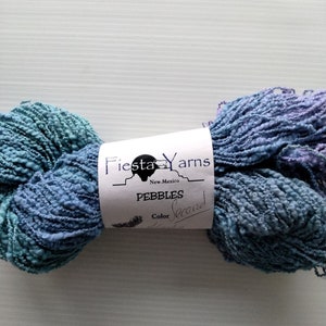 May include: A skein of blue and teal yarn with a textured, nubby appearance. The yarn is labeled "Pebbles" by Fiesta Yarns, New Mexico. The color is labeled "Second".