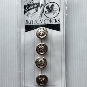 May include: A package of four silver-colored button covers. Each button cover has a raised design in the center. The package has the words "Classic Button Covers" printed on it.