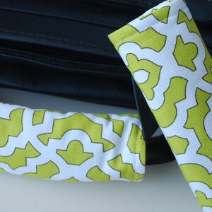 May include: Two padded handle wraps with a white background and a repeating lime green geometric pattern. The wraps are shown next to a black bag, likely for a laptop or briefcase.
