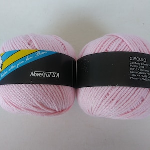 May include: Two balls of pink cotton yarn, each with a black label. The label on the left ball reads "Eston cotton yarn from Brazil Novelsul SA". The label on the right ball reads "CIRCULO Comercio Exterior Ltda PO Box 2004 89010-Blumenau Santa Catarina-Brasil Telex-473-518 CC Phone-473-2271-22".