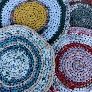 May include: Four round crocheted rugs made from recycled fabric scraps. The rugs are in various colors and patterns, including blue, white, green, yellow, red, and pink.
