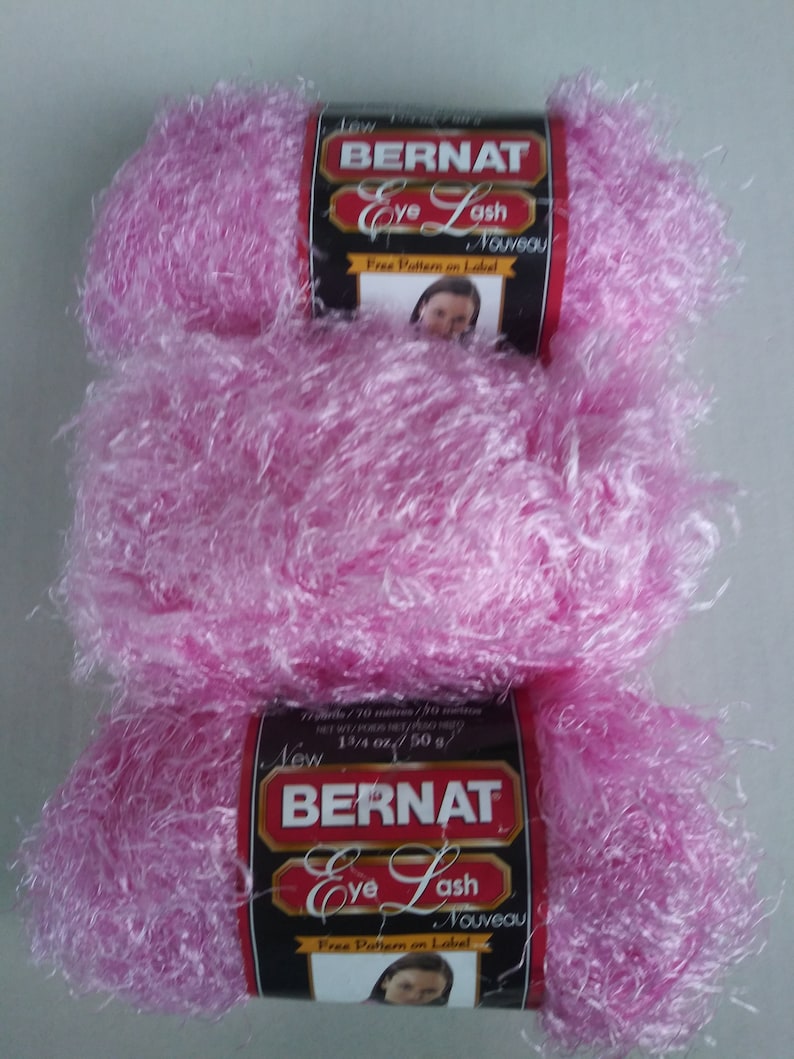 May include: Three skeins of pink Bernat Eye Lash yarn, a soft, fluffy yarn with a fuzzy texture. The yarn label reads "New Bernat Eye Lash Nouveau" and "Free Pattern on Label".