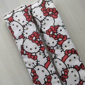 May include: Two white fabric car seat belt pads with a red and black Hello Kitty print.