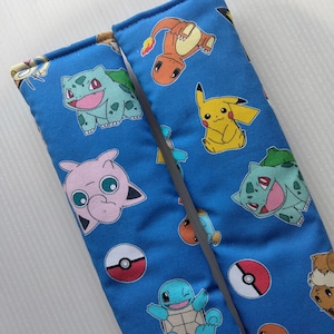May include: Two blue fabric seatbelt pads with a variety of Pokemon characters printed on them. The characters include Pikachu, Bulbasaur, Charmander, Squirtle, and more.