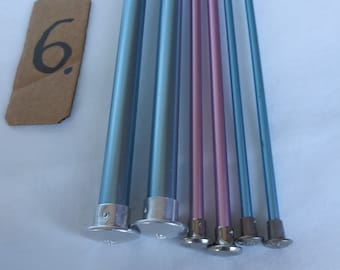 May include: A set of six knitting needles, including two blue, two light blue, and two pink needles. The needles have silver tips and are arranged in a row.