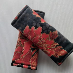 May include: Two black fabric seatbelt covers with a red and gold floral pattern.