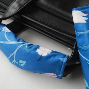 May include: A blue and white floral patterned fabric handle for a bag. The handle is attached to a black leather bag.