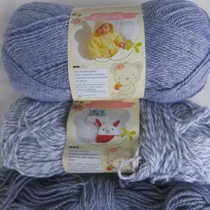 May include: Three skeins of baby yarn in shades of blue and gray. The top skein has a label with a picture of a baby in a yellow hooded jacket. The middle skein has a label with a picture of a bunny hat. The bottom skein is a darker shade of blue.