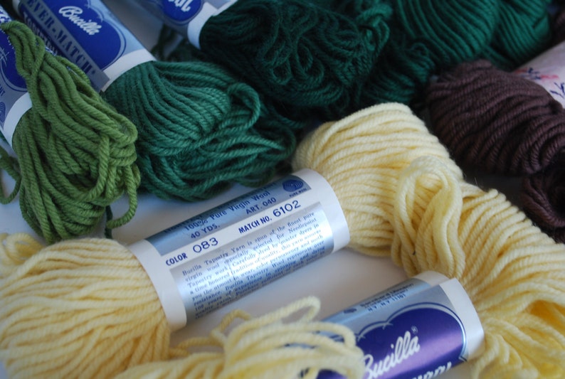May include: Close-up of several spools of Bucilla Ever-Match embroidery floss in various colors, including green, yellow, brown, and white. The spools have labels with the brand name, color number, and yardage.