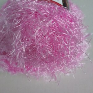 May include: A skein of pink fuzzy yarn with a label that reads "Red Heart Boutique -  Sable -  100% Polyester -  Machine Wash -  Made in USA -  Weight:  Super Fine -  Yardage:  300 -  Suggested Crochet Hook:  H/8 -  Suggested Knitting Needles:  Size 8 -  Content:  100% Polyester -  Care:  Machine Wash -  Made in USA".