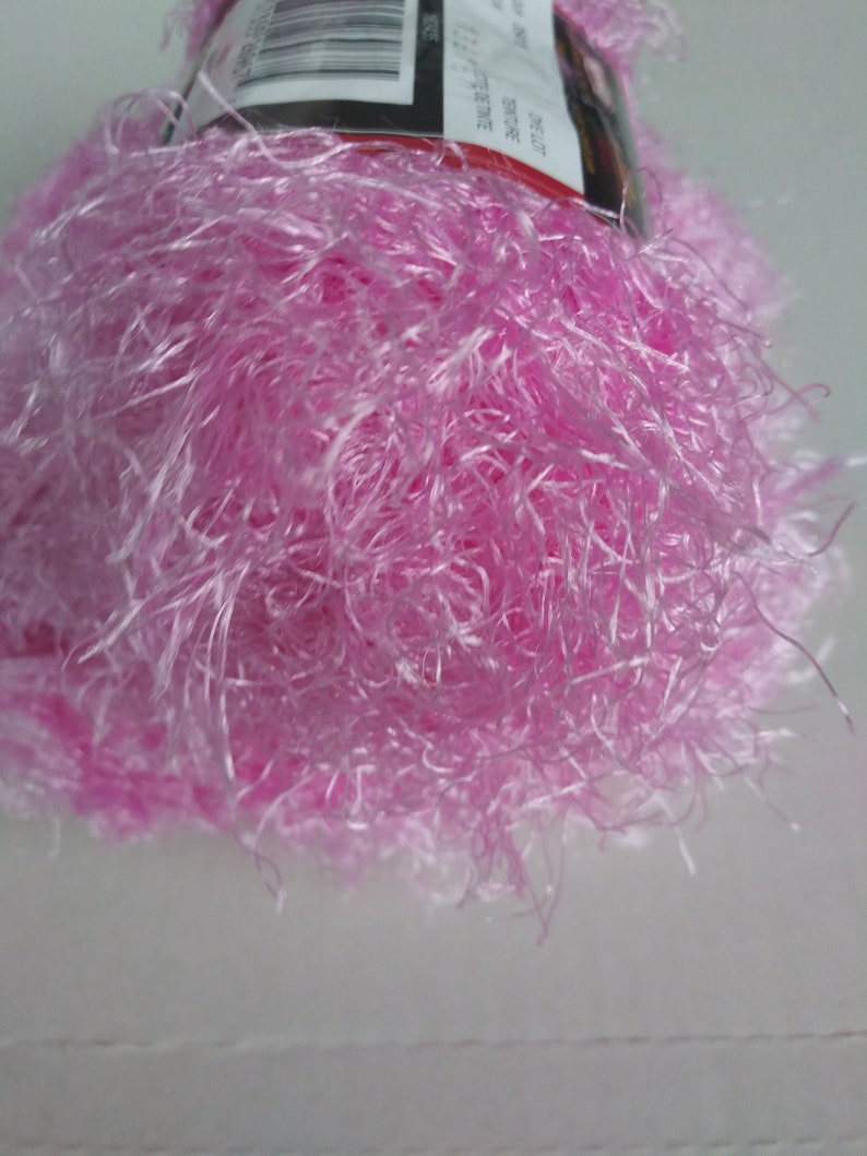 May include: A skein of pink fuzzy yarn with a label that reads "Red Heart Boutique -  Sable -  100% Polyester -  Machine Wash -  Made in USA -  Weight:  Super Fine -  Yardage:  300 -  Suggested Crochet Hook:  H/8 -  Suggested Knitting Needles:  Size 8 -  Content:  100% Polyester -  Care:  Machine Wash -  Made in USA".