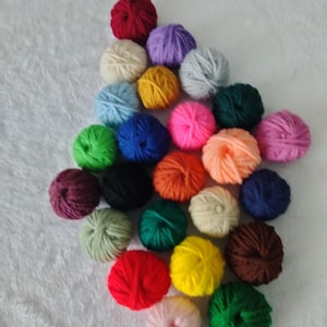 May include: A collection of colorful yarn balls in various shades, including red, yellow, green, blue, and purple. The yarn balls are arranged on a white, textured surface, creating a visually appealing display for crafting projects.