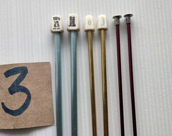 May include: Five knitting needles, two blue, two gold, and one red. The blue needles are labeled "10 1/2 US 6.5 mm" and "Susan Bates". The gold needles are labeled "8" and "Fani".
