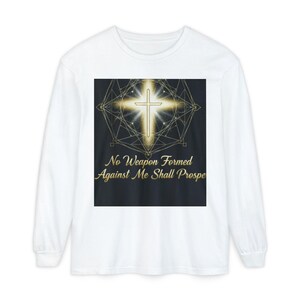 May include: White long-sleeve shirt featuring a gold cross design with a geometric pattern and the text "No Weapon Formed Against Me Shall Prosper." The design is centered on the chest.