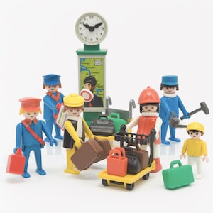 Puede incluir: Un conjunto de figuras de Playmobil que incluye personal de estación y viajeros con equipaje. La escena presenta un reloj de estación verde con un mapa, un carrito de equipaje amarillo, varias maletas en rojo, negro y verde, y figuras con trajes azules, amarillos y rojos.