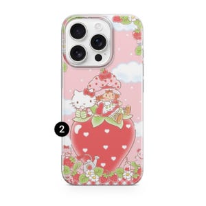 May include: A phone case featuring a pink background with white clouds and a strawberry design. The case has a cartoon illustration of Hello Kitty and a doll sitting on a large strawberry. The case has a clear border.