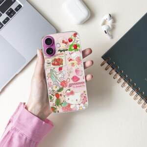 May include: A clear phone case with a pink background featuring a strawberry and floral design. The case has a collage of images, including strawberries, flowers, and a cartoon character. The text "Strawberries" is visible on the case.