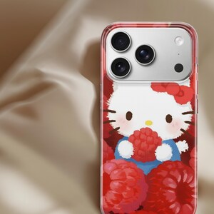 May include: Clear phone case featuring a cartoon image of Hello Kitty holding a raspberry. The case has a red border and a background filled with red raspberries. The phone's camera lenses are visible at the top.