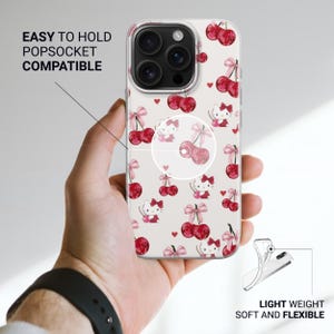 May include: A clear phone case with a pattern of red cherries, bows, and a cartoon cat character. The case is held in a hand and has the text "EASY TO HOLD POPSOCKET COMPATIBLE" and "LIGHT WEIGHT SOFT AND FLEXIBLE".