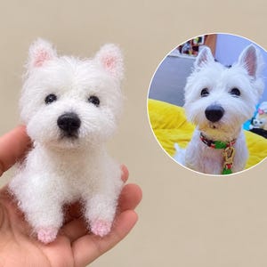 May include: A small, white, fuzzy, crocheted West Highland White Terrier figurine with black eyes and a black nose. Beside it is a circular inset photograph of a real white dog wearing a colourful collar, matching the appearance of the figurine.