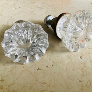 May include: Two clear glass door knobs with a faceted design. The knobs are attached to metal bases.