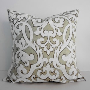May include: A decorative throw pillow with a beige and white damask pattern. The pillow has a square shape and a soft, plush texture.