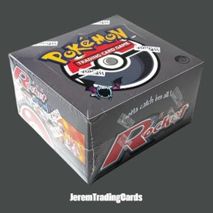 May include: A sealed Pokémon Trading Card Game Team Rocket booster box featuring the yellow and blue Pokémon logo, a black and white Poké Ball graphic, a purple Zubat illustration, and the text Gotta catch 'em all! and Team Rocket.