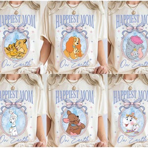 May include: Cream-colored t-shirts with the text "Happiest Mom On Earth" in light blue. Each shirt features a different cartoon image inside an oval frame with a bow. The images include a lion family, a dog family, and an elephant.