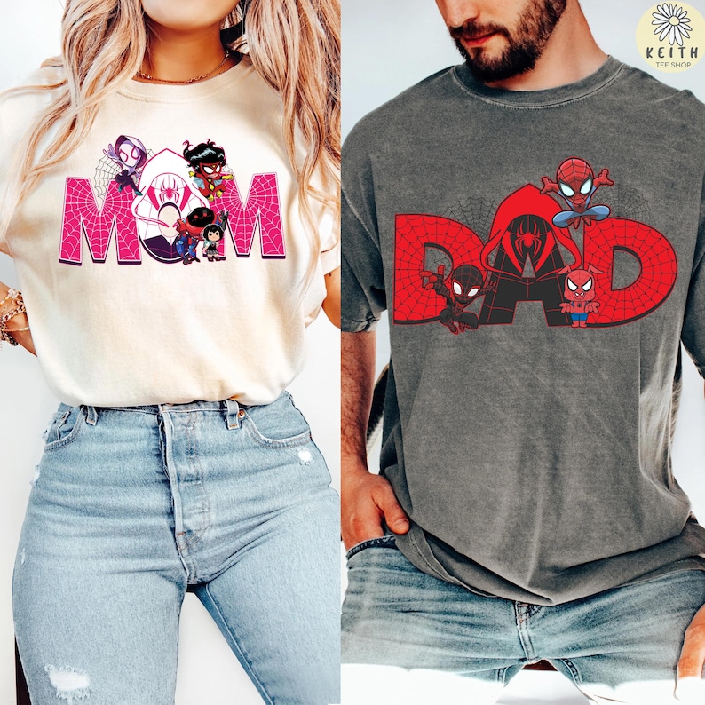 May include: Two t-shirts, one cream-colored and one gray, featuring superhero-themed graphics. The cream shirt says "MOM" in pink with cartoon characters. The gray shirt says "DAD" in red with Spider-Man characters. Both shirts are short-sleeved.