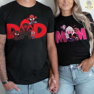 May include: Black t-shirts with Spider-Man graphics. One shirt features the word "DAD" in red with Spider-Man characters. The other shirt displays "MOM" in pink, also with Spider-Man characters. Both shirts are worn by people.