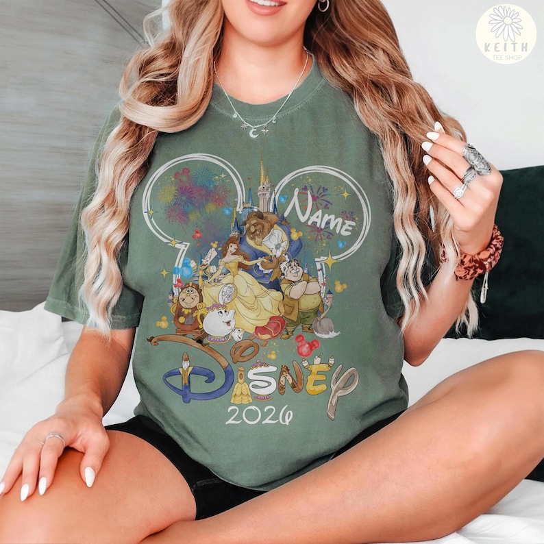 May include: Green t-shirt featuring a Disney-themed graphic with the text "Disney 2020". The design includes characters from Beauty and the Beast, fireworks, and a castle. The word "Name" is also present in the design.