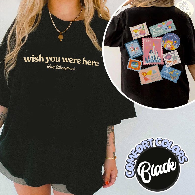 May include: Black t-shirt with the text "wish you were here" and "Walt Disney World" in a cream color. The back of the shirt features several colorful postage stamp-like patches with Disney-themed designs. The shirt is part of the Comfort Colors collection.