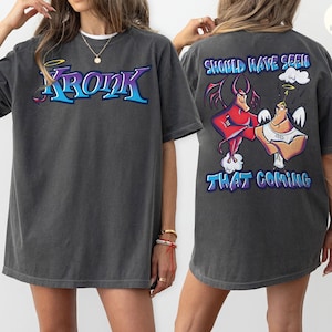 May include: Dark gray t-shirt with the word "Kronk" in blue and teal lettering on the front. The back of the shirt features a cartoon illustration of two characters with the text "Should Have Seen That Coming".