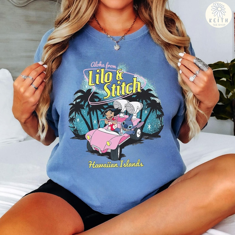 May include: A blue t-shirt featuring a graphic of Lilo and Stitch in a pink car with palm trees and the text "Aloha from Lilo & Stitch Hawaiian Islands". The shirt has a crew neck and short sleeves.