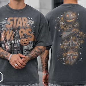 Può includere: Una t-shirt grigio antracite con una grafica di Halloween a tema Star Wars. Il davanti mostra Darth Vader con un secchiello a forma di zucca e degli Stormtrooper. Il retro presenta una Morte Nera a zucca, un distruttore e navi spaziali.