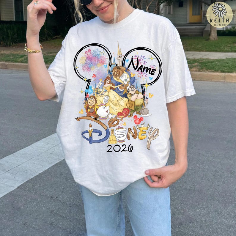 May include: White t-shirt featuring a colorful Disney graphic with the text "Disney 2026" and a customizable name. The design includes characters from Beauty and the Beast, fireworks, and a castle.