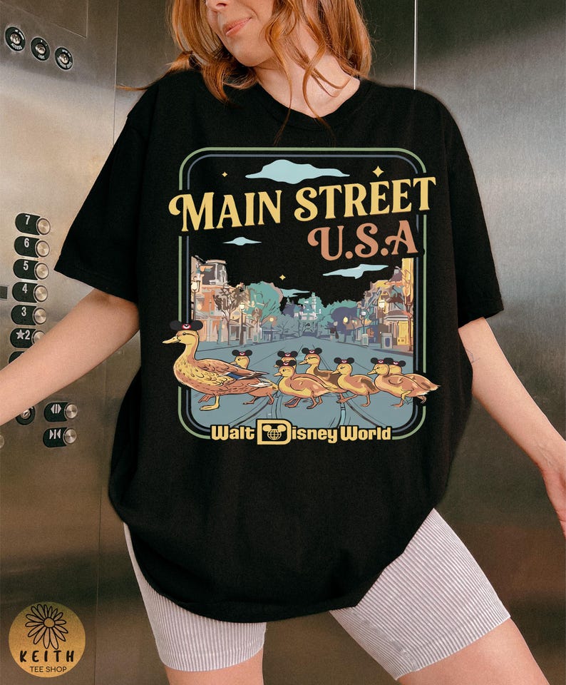 May include: Black t-shirt with a vintage-style design of Main Street U.S.A. featuring a duck family wearing hats. The graphic includes the text "Main Street U.S.A." and "Walt Disney World".