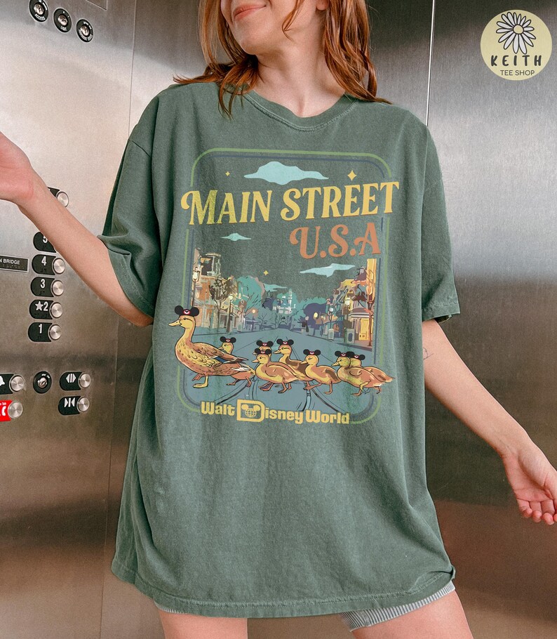 May include: Green t-shirt with a graphic showing "Main Street U.S.A." above a street scene and ducks wearing Mickey Mouse ears. The text "Walt Disney World" is below the graphic.