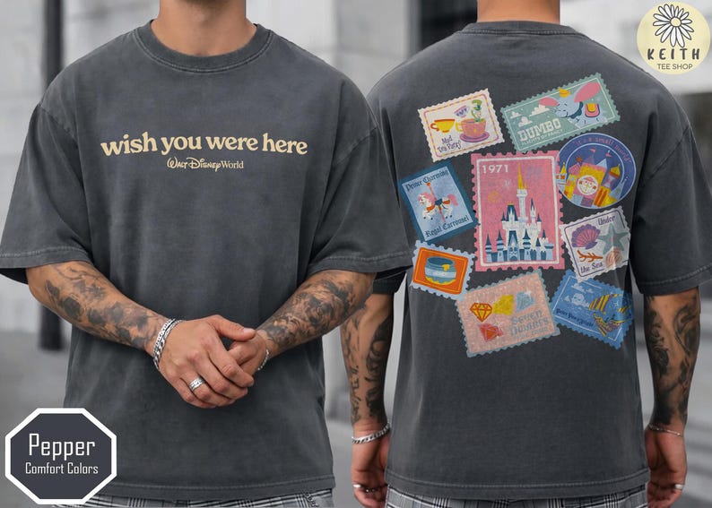 May include: Dark gray t-shirt with "wish you were here" and "Walt Disney World" text. The back features colorful postage stamp designs with Disney themes. The shirt is a Pepper Comfort Colors brand.