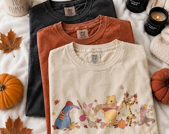 Puede incluir: Tres camisetas de cuello redondo en gris carbón, óxido y crema. La camiseta crema presenta un estampado gráfico de Igor, Piglet, Winnie the Pooh, Tigger y Rito rodeados de hojas de otoño y una calabaza. Cada camiseta tiene una etiqueta Comfort Colors.