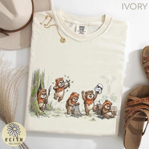 May include: Ivory-colored sweatshirt featuring a whimsical illustration of Ewoks in a forest setting. The graphic shows several Ewoks with weapons and a Stormtrooper helmet. The shirt has the text "COMFORT COLORS" and "KEITH TEE SHOP".