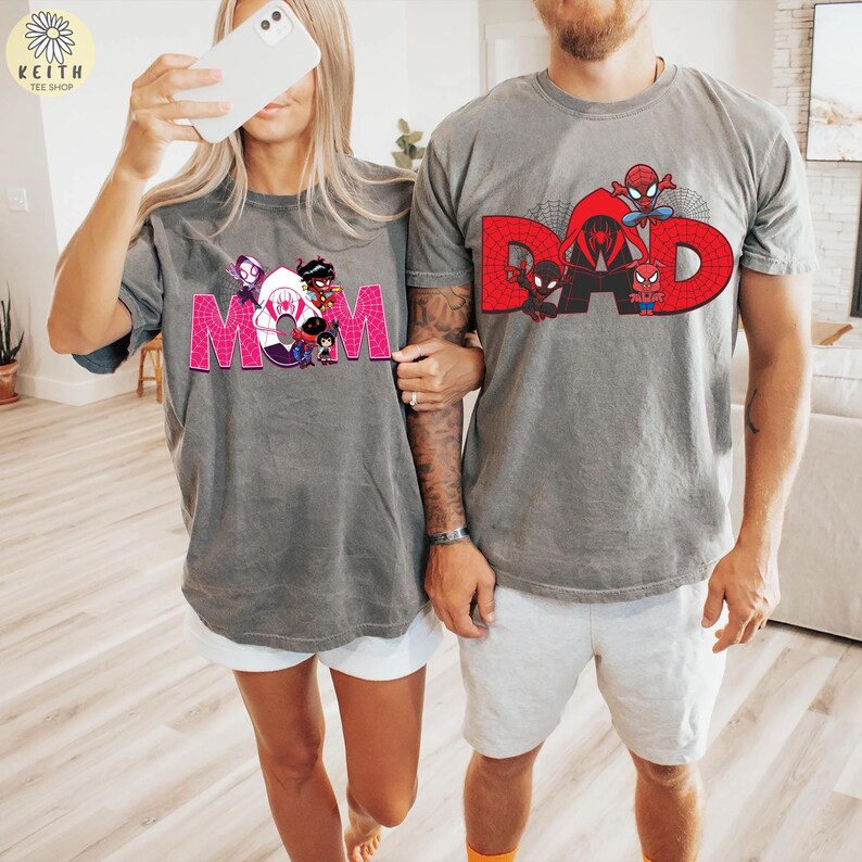 May include: Two gray t-shirts with matching designs. One shirt says "MOM" in pink block letters with cartoon characters. The other shirt says "DAD" in red block letters with cartoon Spider-Man characters. Both shirts are short-sleeved.