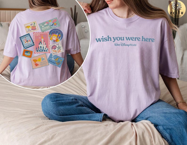 May include: A light purple t-shirt with the text "wish you were here" and "Walt Disney World" printed in blue. The back of the shirt features a collection of colorful postage stamp designs with various illustrations and the year 1971.