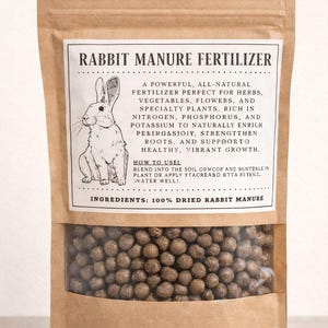 May include: A brown paper bag of rabbit manure fertilizer. The bag has a clear window showing the pelletized fertilizer. The label reads "Rabbit Manure Fertilizer" with a drawing of a rabbit.