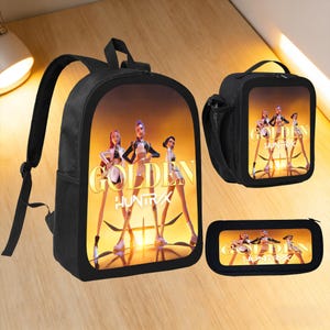 Może przedstawiać: Czarny zestaw plecaka, torby na lunch i piórnika. Każdy element zawiera grafikę trzech postaci z napisem "GOLDEN HUNTRX" w kolorze złotym. Tło to gradient żółtego i pomarańczowego.