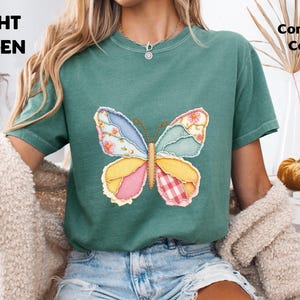May include: A light green short-sleeve t-shirt featuring a central graphic of a butterfly composed of various patterned fabric patches in shades of blue, yellow, pink, and white. The text LIGHT GREEN and Comfort Colors appears in the corners.